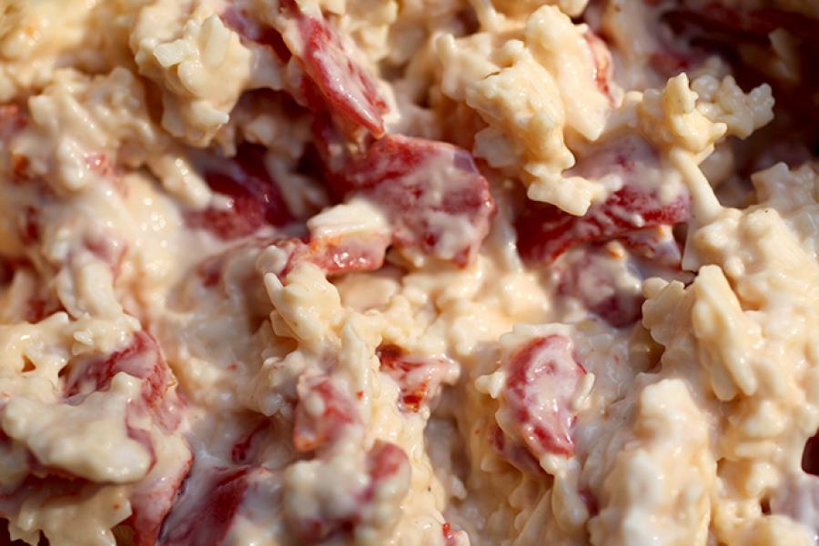 Close-up view of creamy pimento cheese dip garnished with made with shredded cheese, chopped pimentos and mayonnaise.